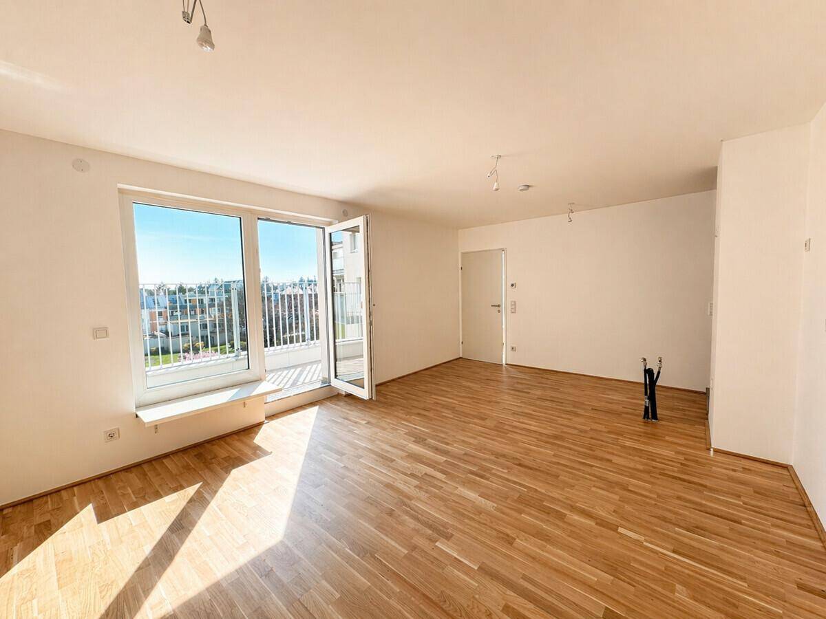 Geräumiges, helles Zimmer mit Holzboden und großen Fenstern, die auf einen Balkon mit Stadtblick führen.