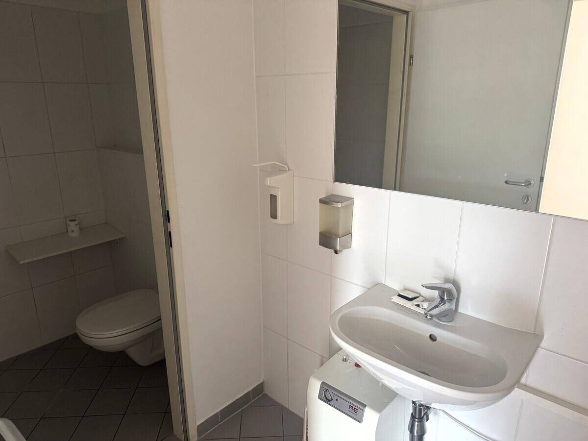 Geflieste Toilette mit Waschbecken und Spiegel, in einem gepflegten und funktionalen Zustand.