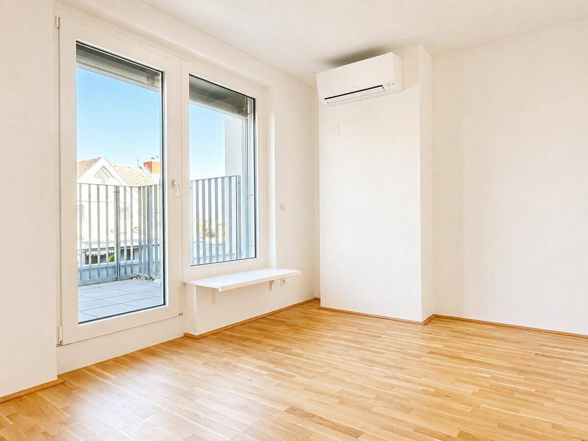 Lichtdurchfluteter Raum mit Parkettboden, Klimaanlage und Zugang zu einem Balkon oder einer Terrasse.