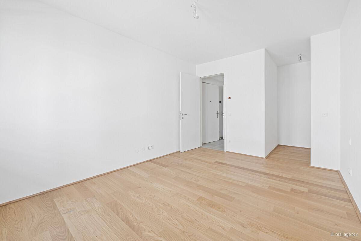 Leeres Zimmer mit Holzboden und weiß gestrichenen Wänden, bereit zur Einrichtung.