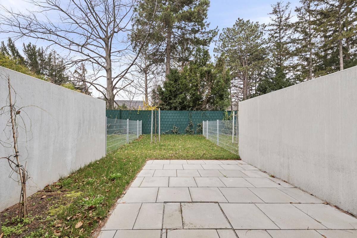 Kleiner, umzäunter Gartenbereich mit gepflasterter Terrasse und grüner Hecke im Hintergrund.