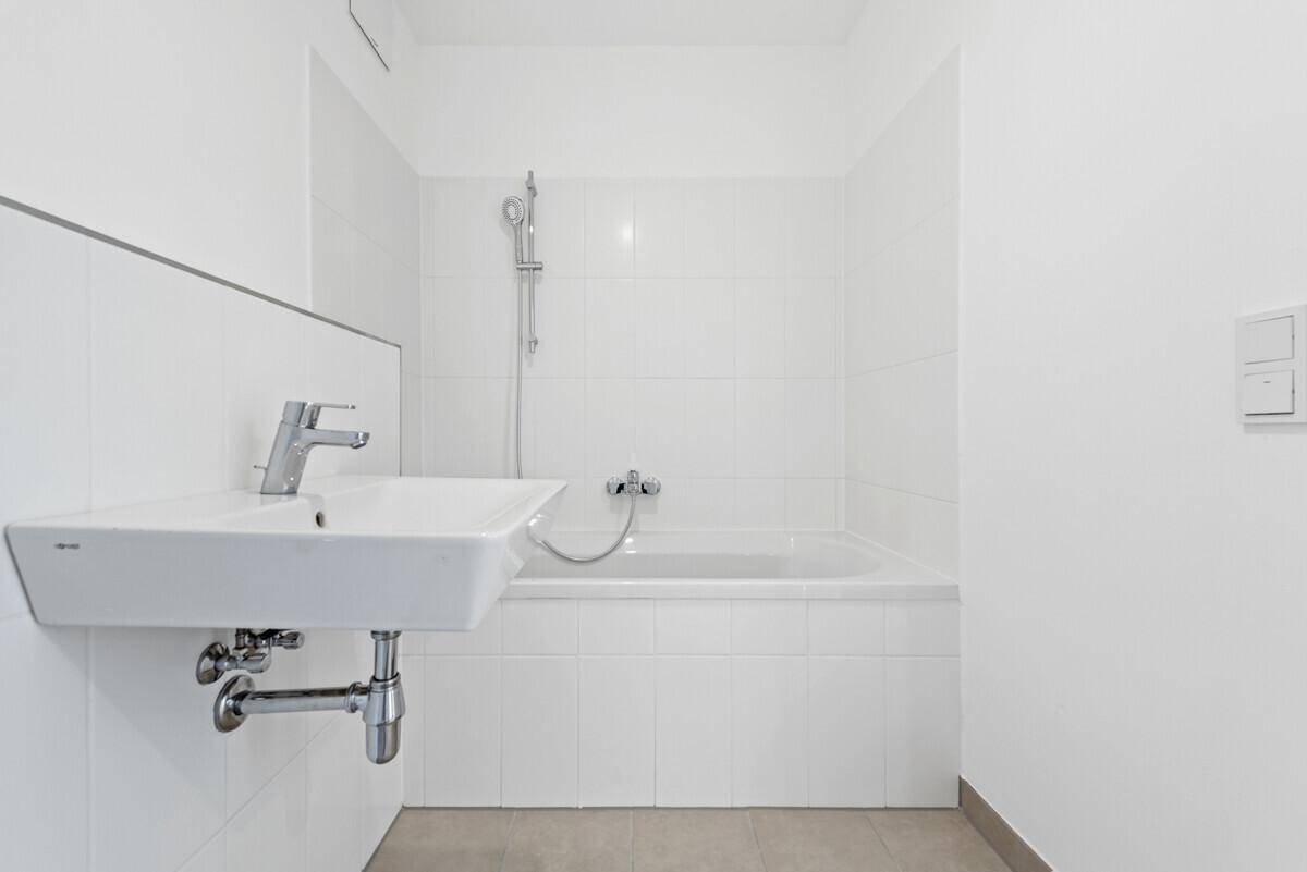 Modernes Badezimmer mit weiß gefliesten Wänden, Waschbecken und einer Badewanne mit Duschfunktion.