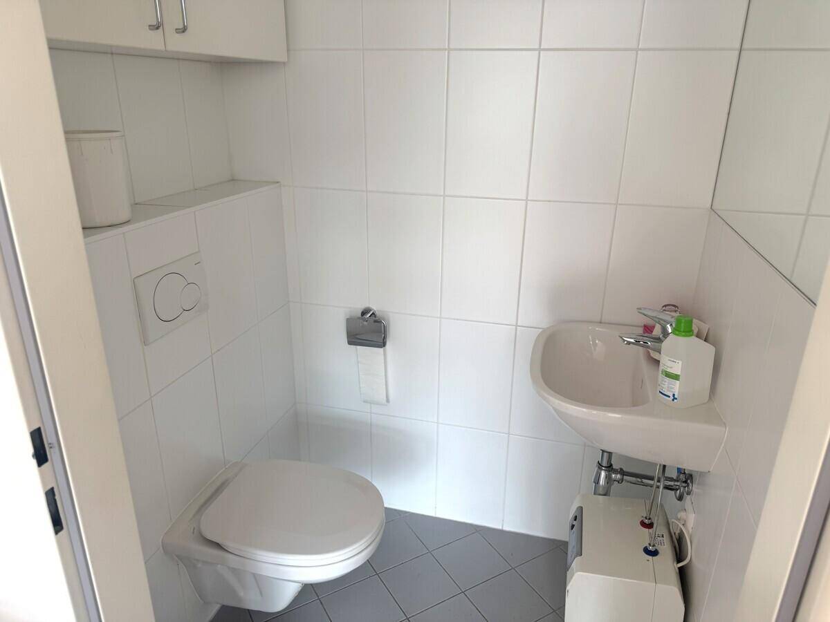 Saubere, geflieste Toilette mit wandhängendem WC und kleinem Waschbecken, in gutem Zustand.