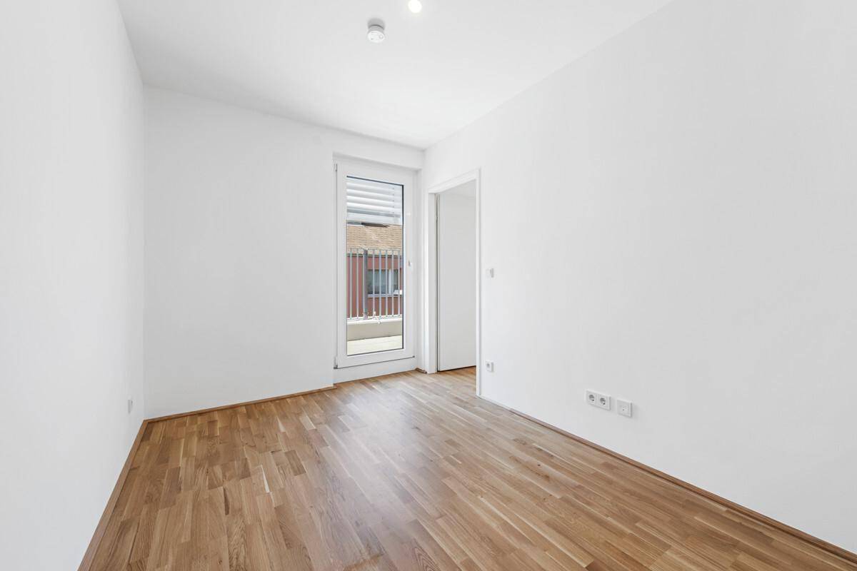 Helles Schlafzimmer mit Parkettboden und direktem Zugang zu einem kleinen Balkon.