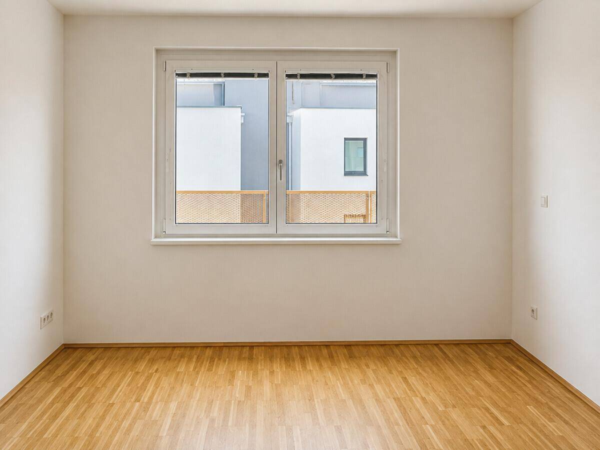 Heller Raum mit Parkettboden und großem Fenster, bietet viel Tageslicht und eine neutrale Gestaltung.