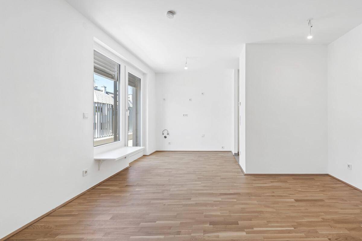 Großer, leerer Wohnraum mit hellem Parkettboden und vorbereiteten Anschlüssen an der Wand.