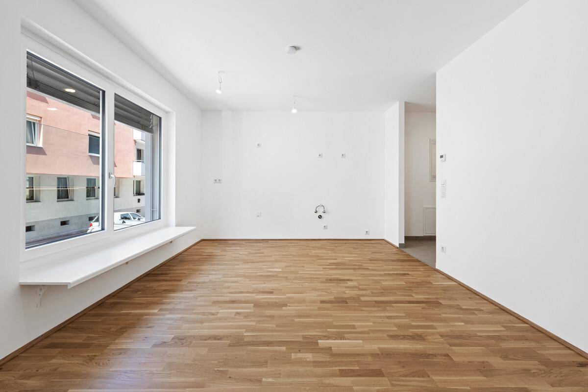Geräumiges, helles Zimmer mit Holzboden und großem Fenster, bereit für individuelle Gestaltung.