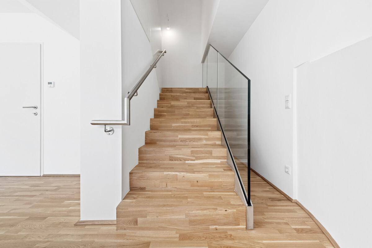 Moderne Holztreppe mit Glasgeländer und Edelstahlhandlauf, die die Etagen verbindet.