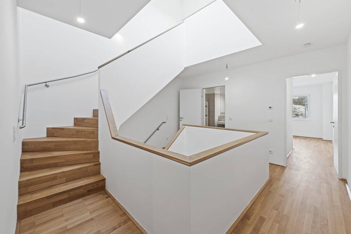 Moderner Treppenaufgang mit Holzstufen und viel Tageslicht von oben.