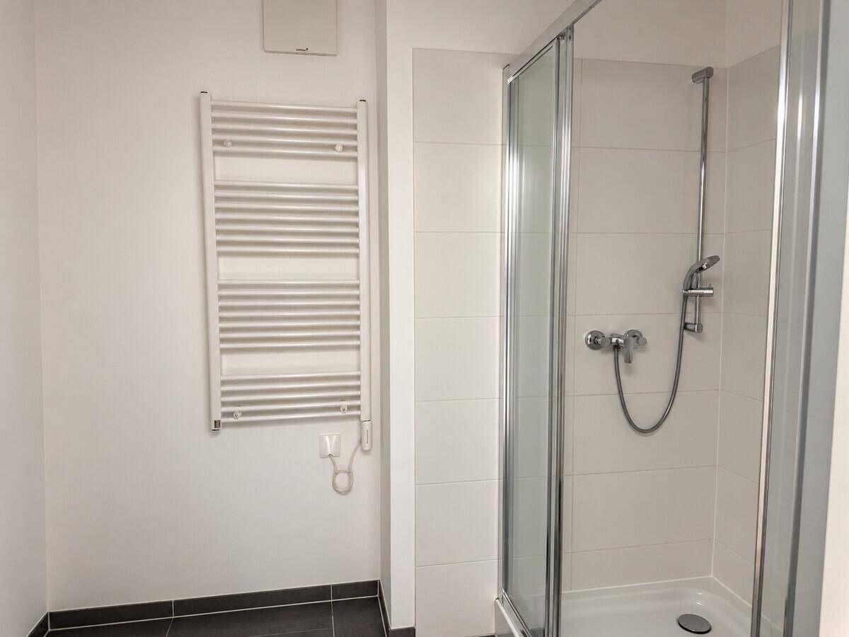 Modernes Badezimmer mit Duschkabine, beheiztem Handtuchhalter und dunklen Bodenfliesen.