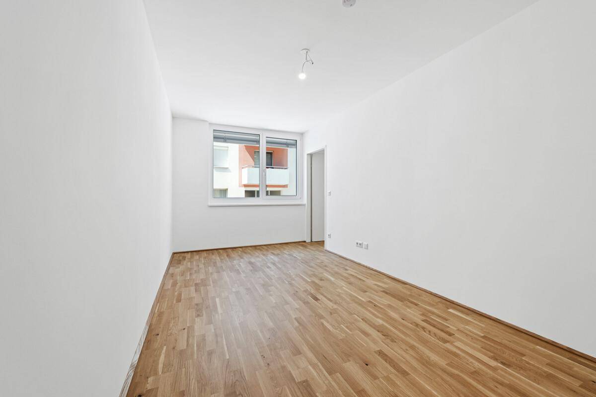 Ruhiges Schlafzimmer mit Parkettboden und großem Fenster, ideal für erholsame Nächte.