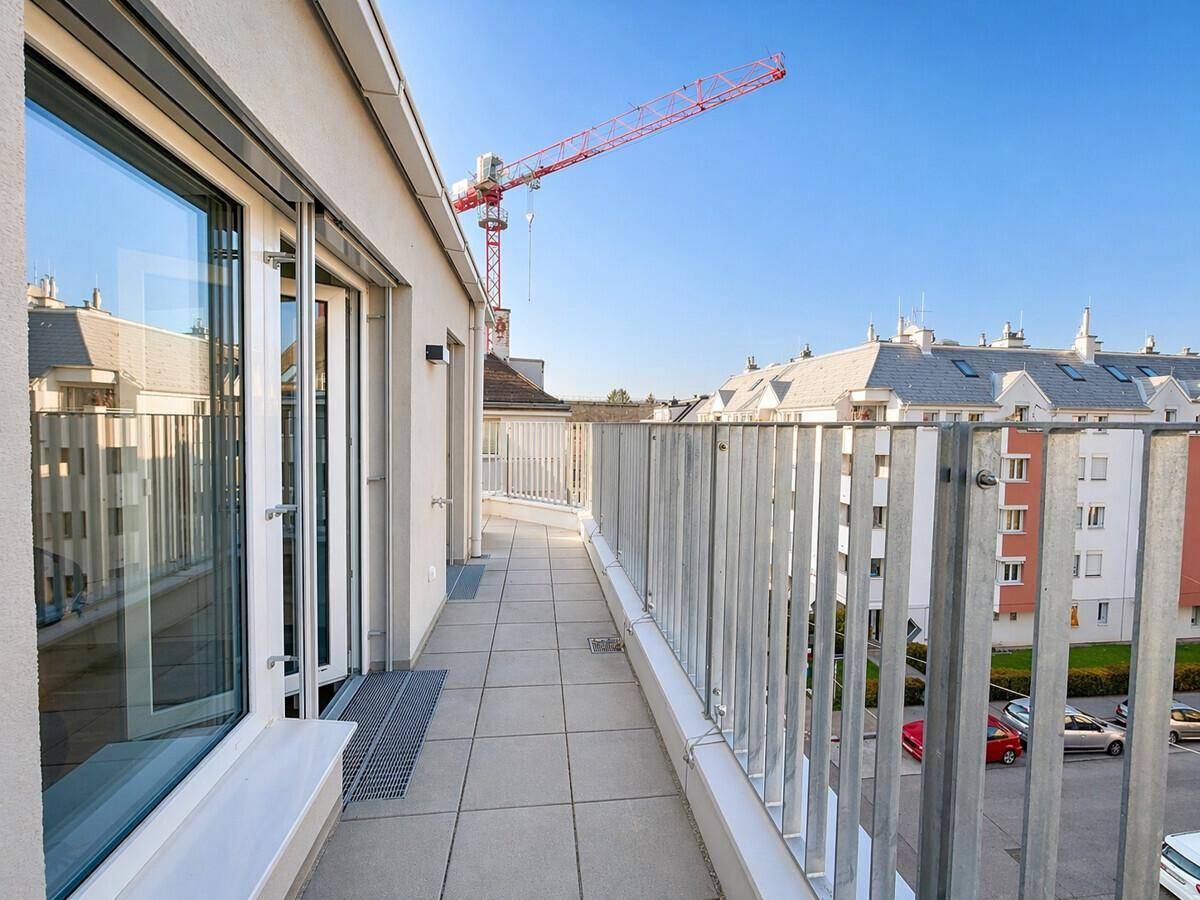 Langer Balkon mit Fliesenboden und Metallgeländer, bietet einen Blick auf die Umgebung und einen Kran.