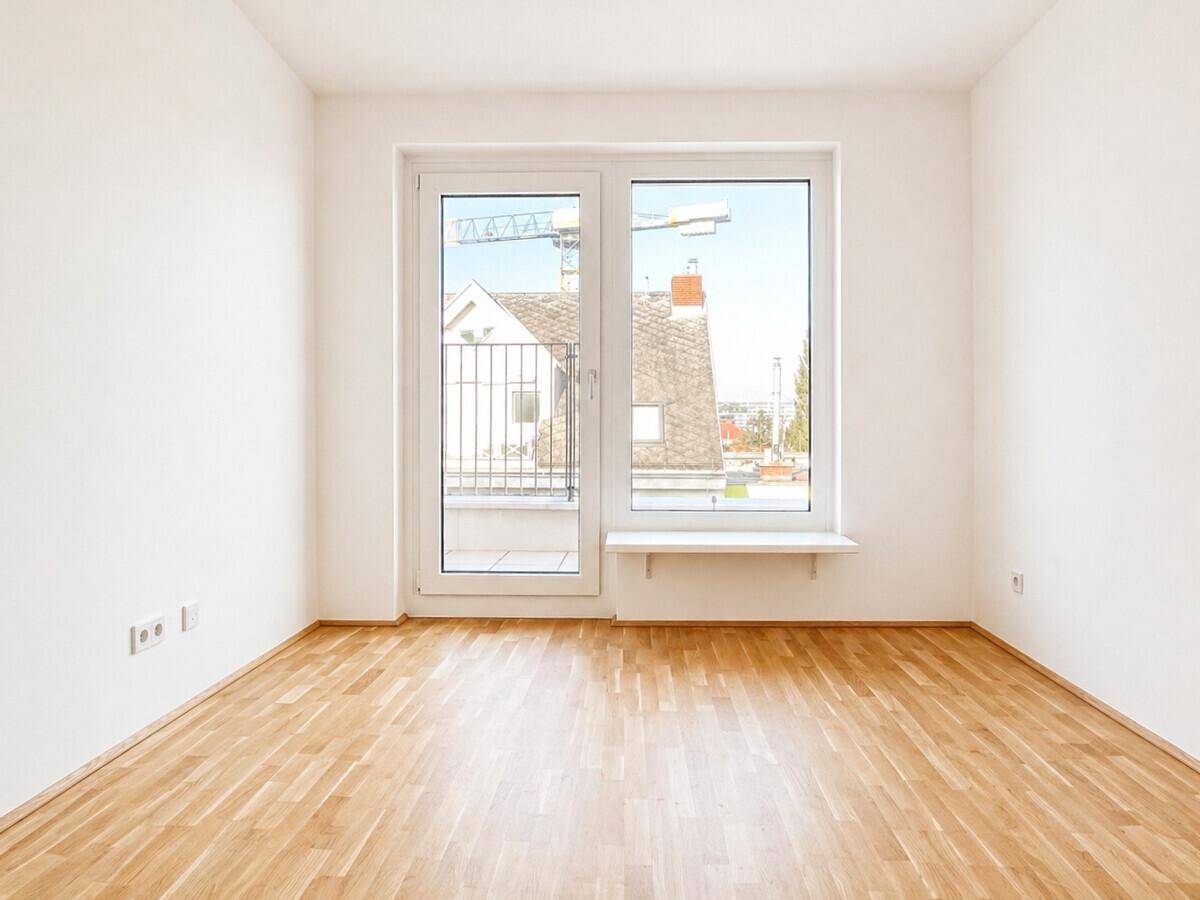 Helles Schlafzimmer mit Parkettboden und großer Balkontür, die viel Tageslicht hereinlässt.