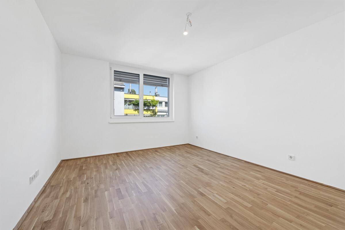 Unmöbliertes Zimmer mit Holzboden und großem Fenster, bereit zur individuellen Gestaltung.