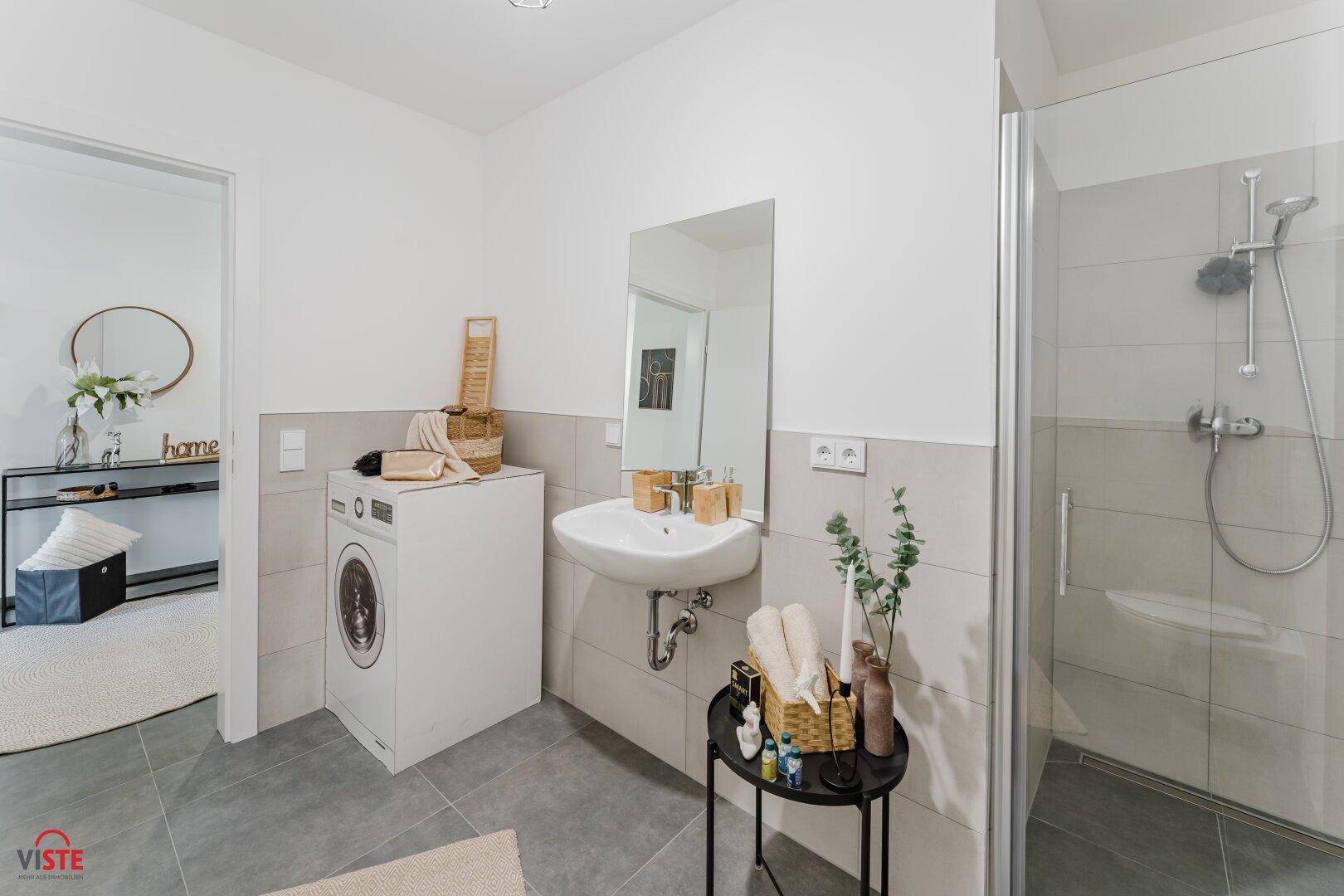 Modernes Badezimmer mit Duschkabine, Waschbecken und integrierter Waschmaschine.
