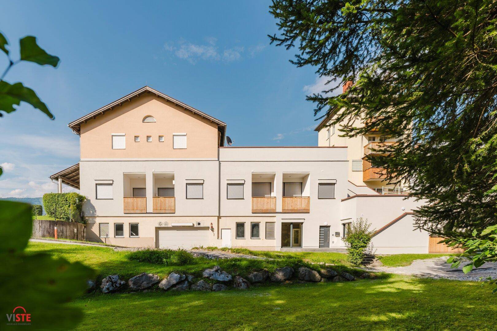 Moderne Wohnhausfassade mit Balkonen, umgeben von einer grünen Gartenanlage.