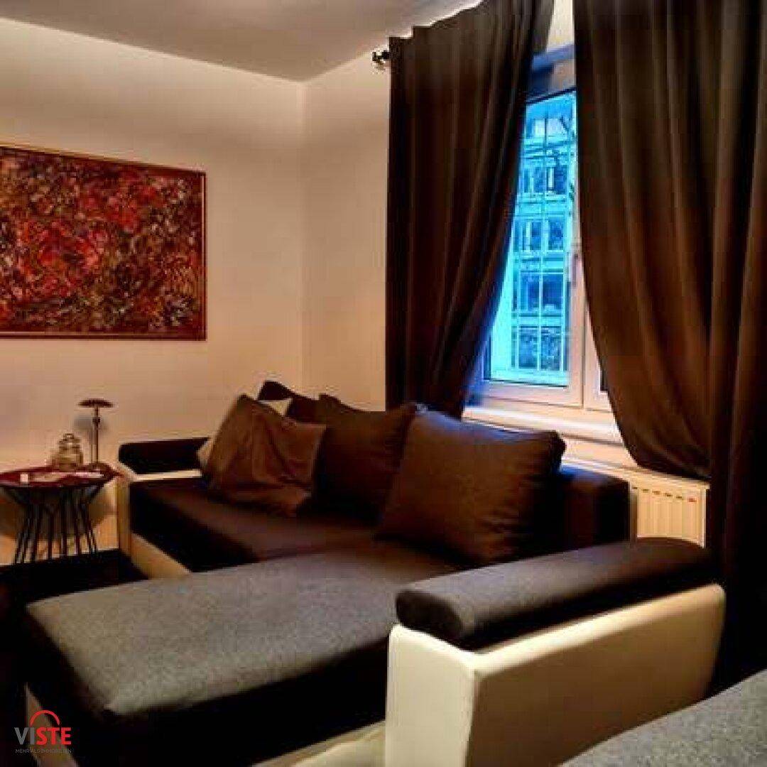 Gemütliches Wohnzimmer mit dunklem Sofa, Vorhängen und einem farbenfrohen Kunstwerk an der Wand.
