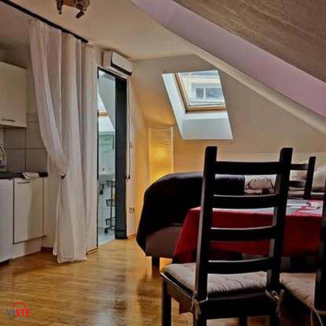 Dachgeschoss-Schlafzimmer mit Holzboden, Dachfenster und einer kleinen Küchenzeile im Hintergrund.
