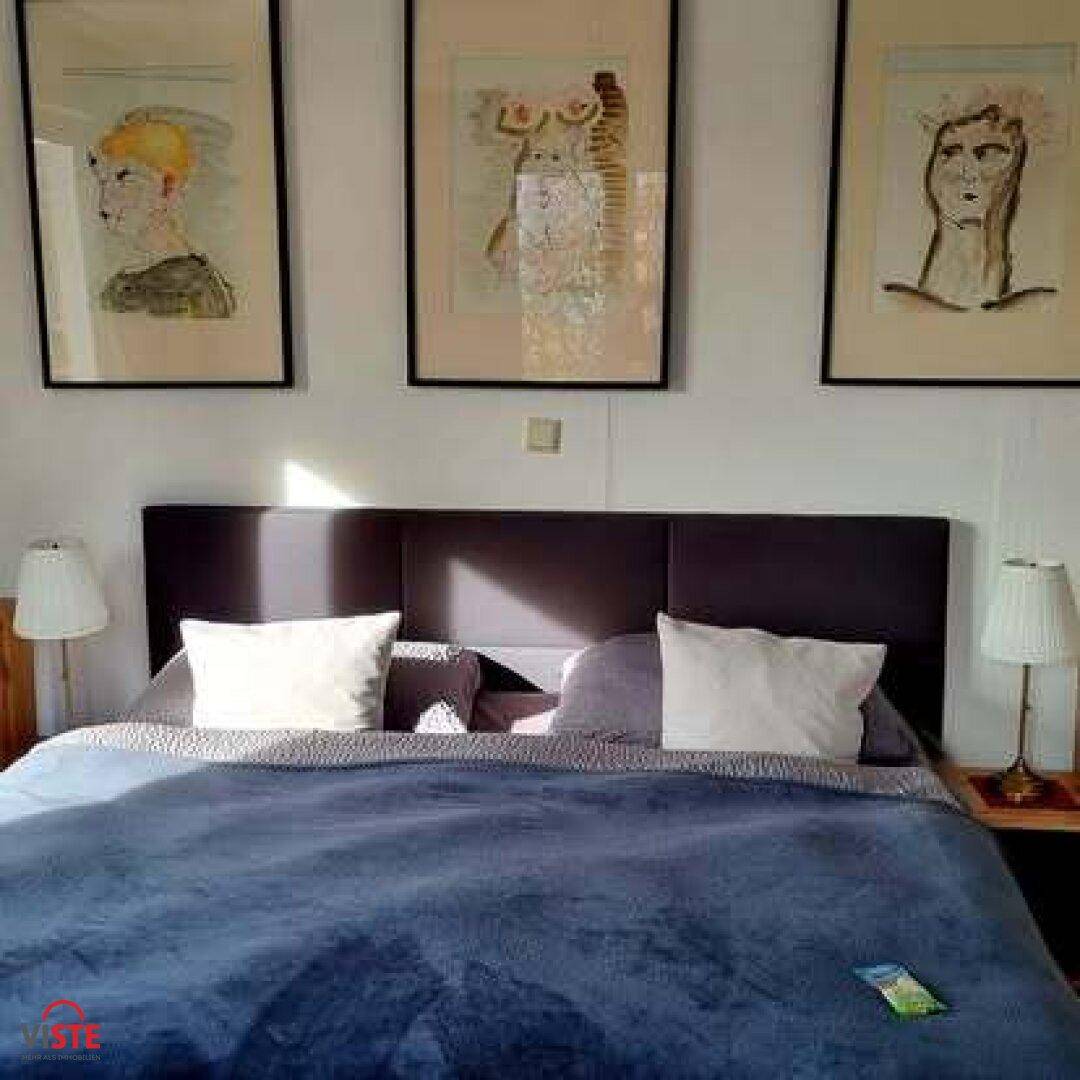 Helles Schlafzimmer mit Doppelbett, Nachttischen und modernen Kunstwerken über dem Kopfteil.