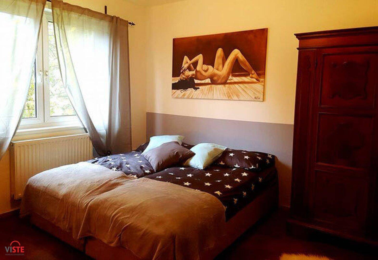 Schlafzimmer mit zwei Einzelbetten, einem Holzschrank und einem Fenster mit hellen Vorhängen.