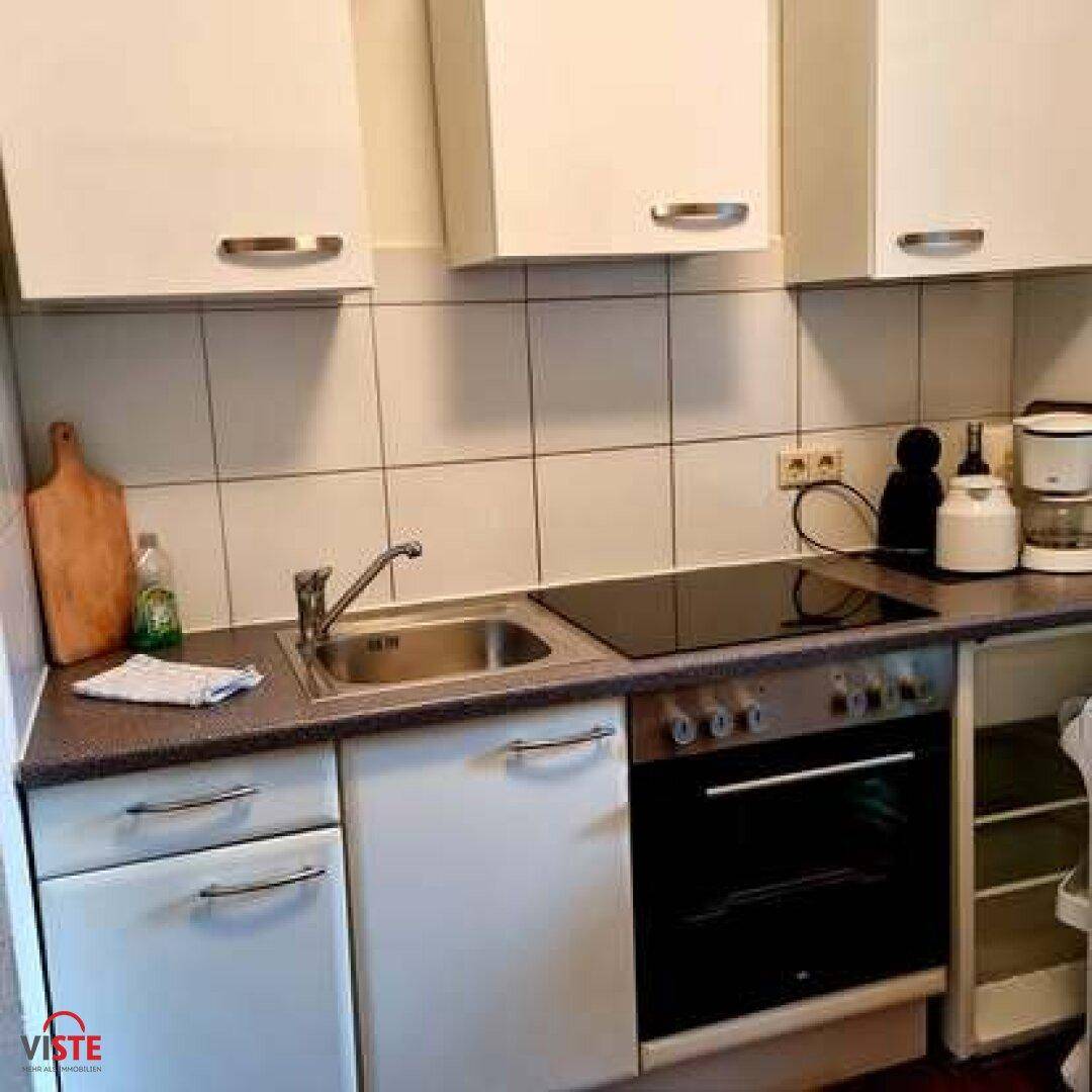 Kleine Küche mit weißen Schränken, Fliesenrückwand und integrierten Kochgeräten.