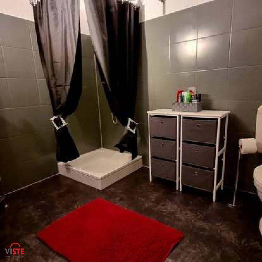 Badezimmer mit dunklen Fliesen, Duschbereich mit Vorhang und einem kleinen Regal.