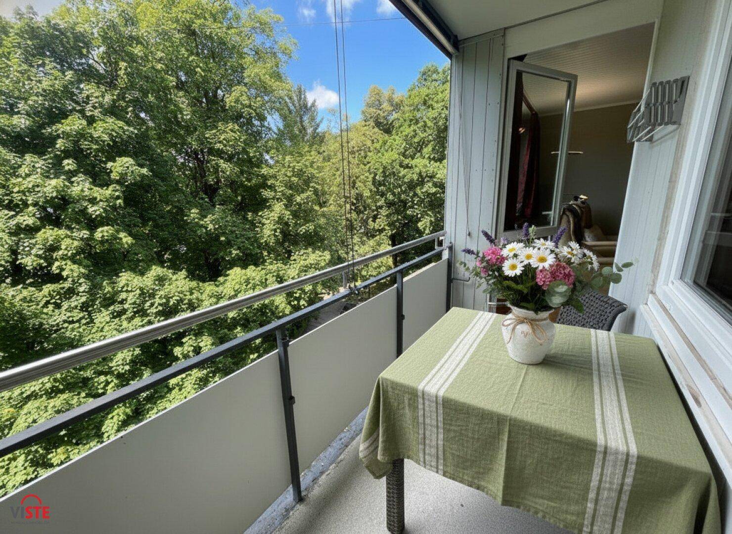 Sonnenverwöhnter Balkon mit Tisch und Stühlen, umgeben von üppigem Grün.
