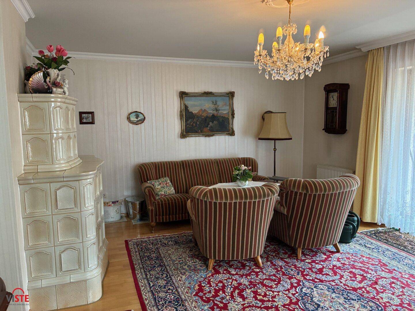 Gemütliches Wohnzimmer mit Kachelofen, Kronleuchter und traditioneller Einrichtung.