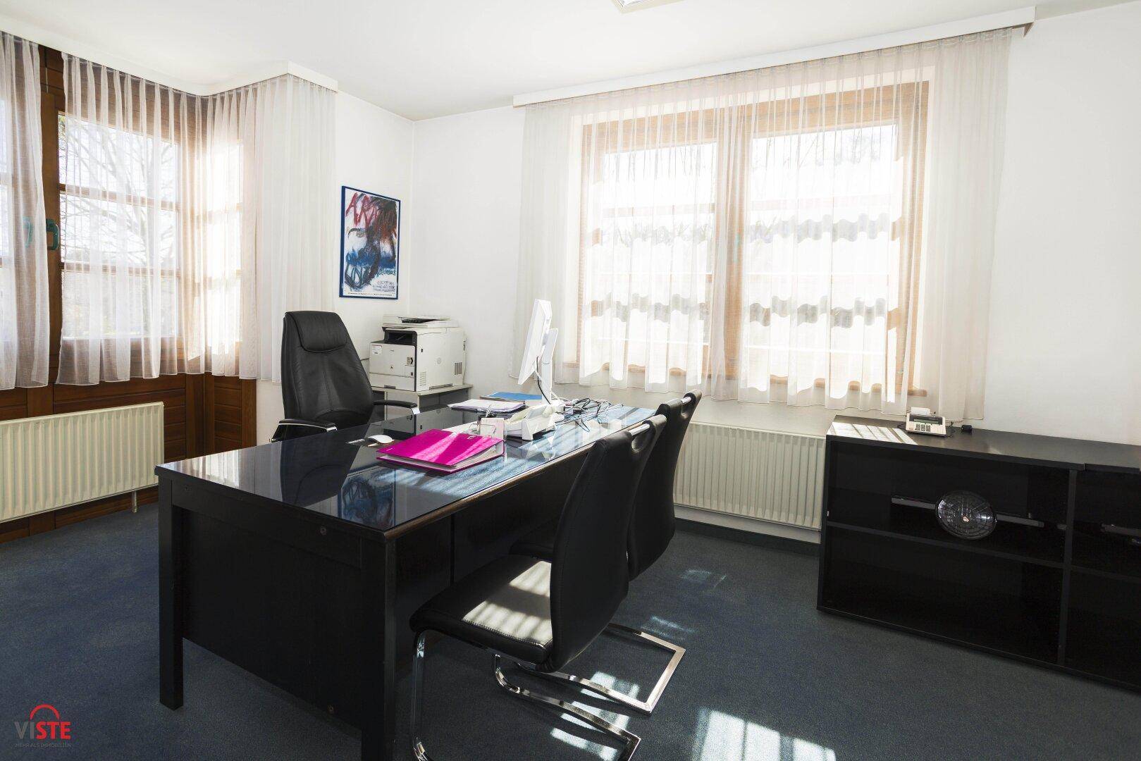 Geräumiges Büro mit einem großen Schreibtisch, Bürostühlen und einem Fenster, das viel Licht hereinlässt.