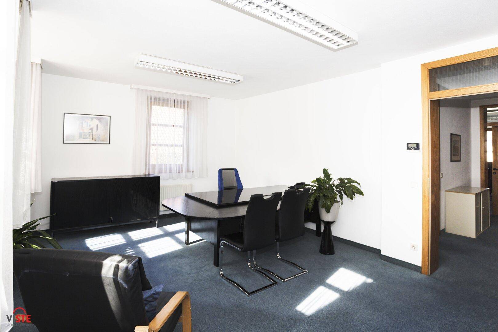 Helles Büro mit einem großen Besprechungstisch, Bürostühlen und einem Blick auf den Flur.