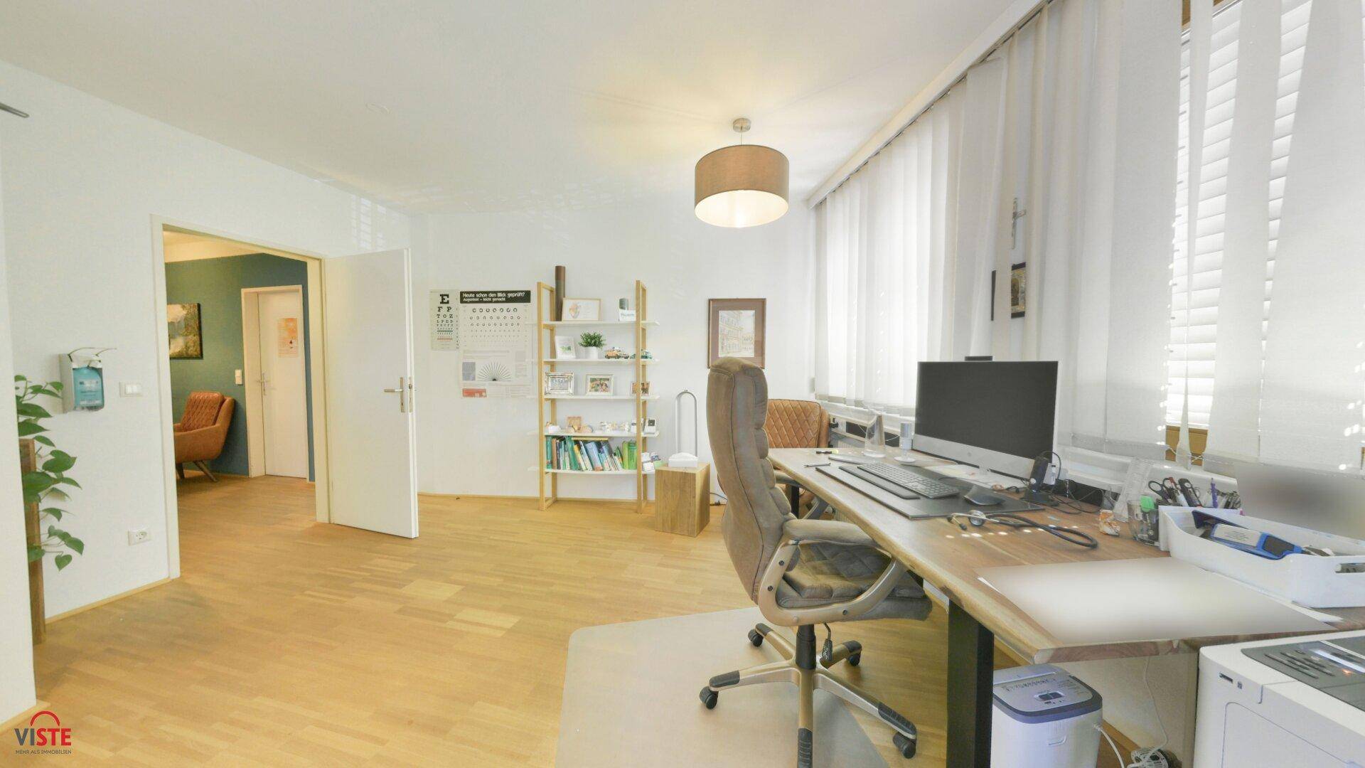 Geräumiges Büro mit Holzschreibtisch, Computerarbeitsplatz und Regalen, verbunden durch eine offene Tür.