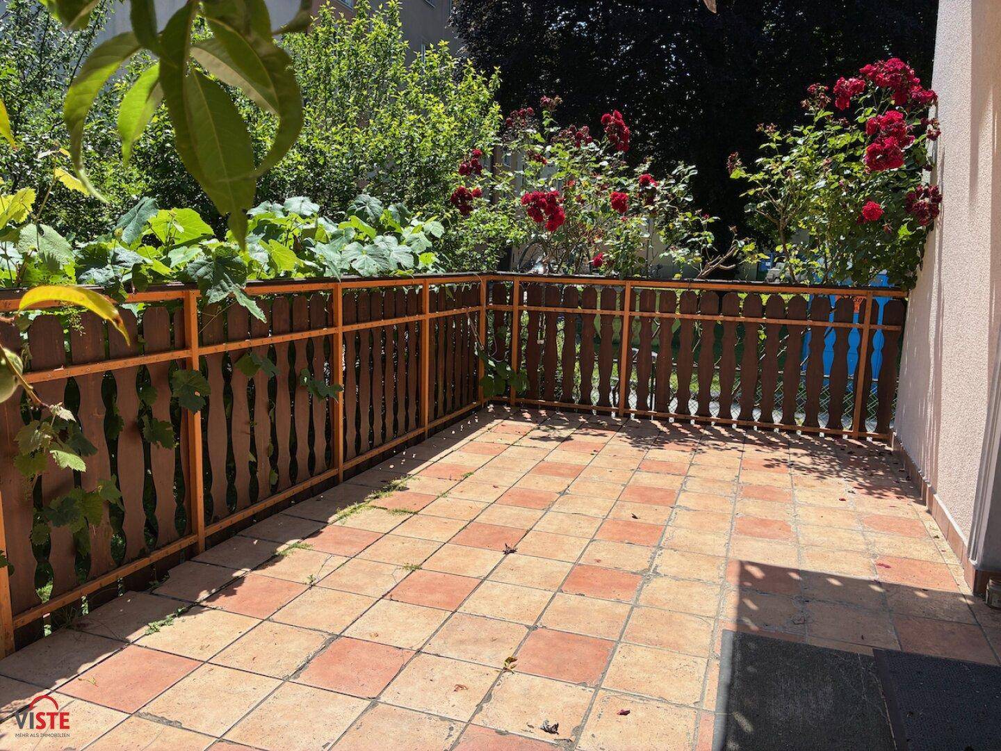 Geflieste Terrasse mit Holzzaun und blühenden roten Rosen, ideal für entspannte Stunden.