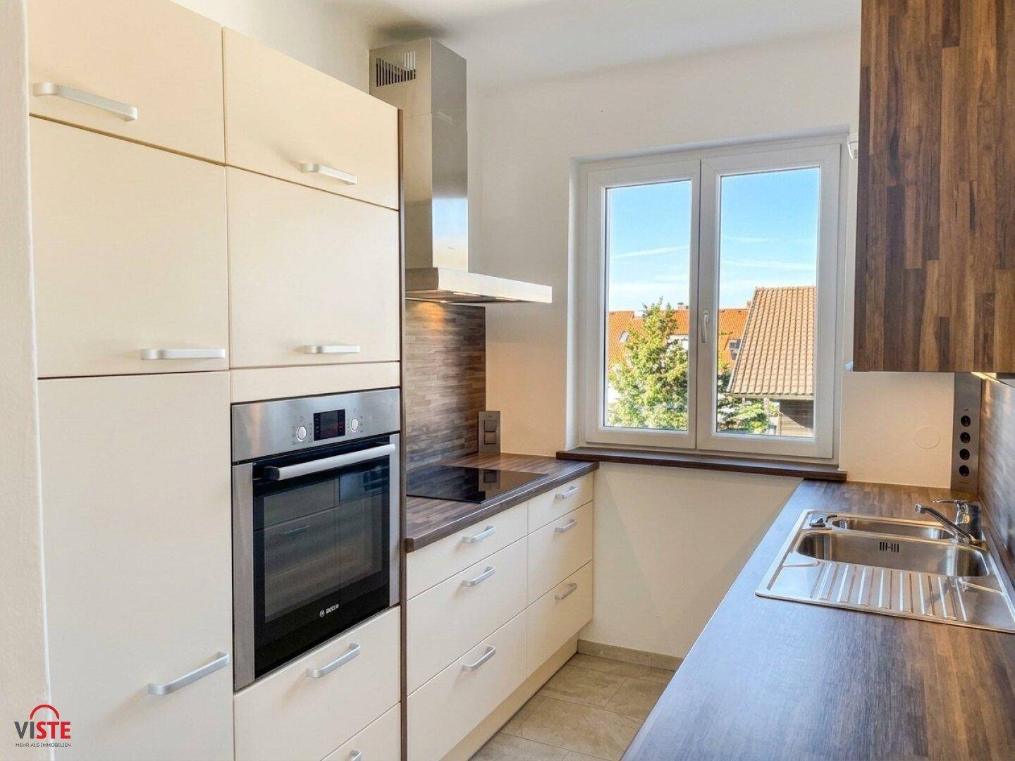 Moderne Einbauküche mit hellen Fronten, integriertem Backofen und Fensterblick.