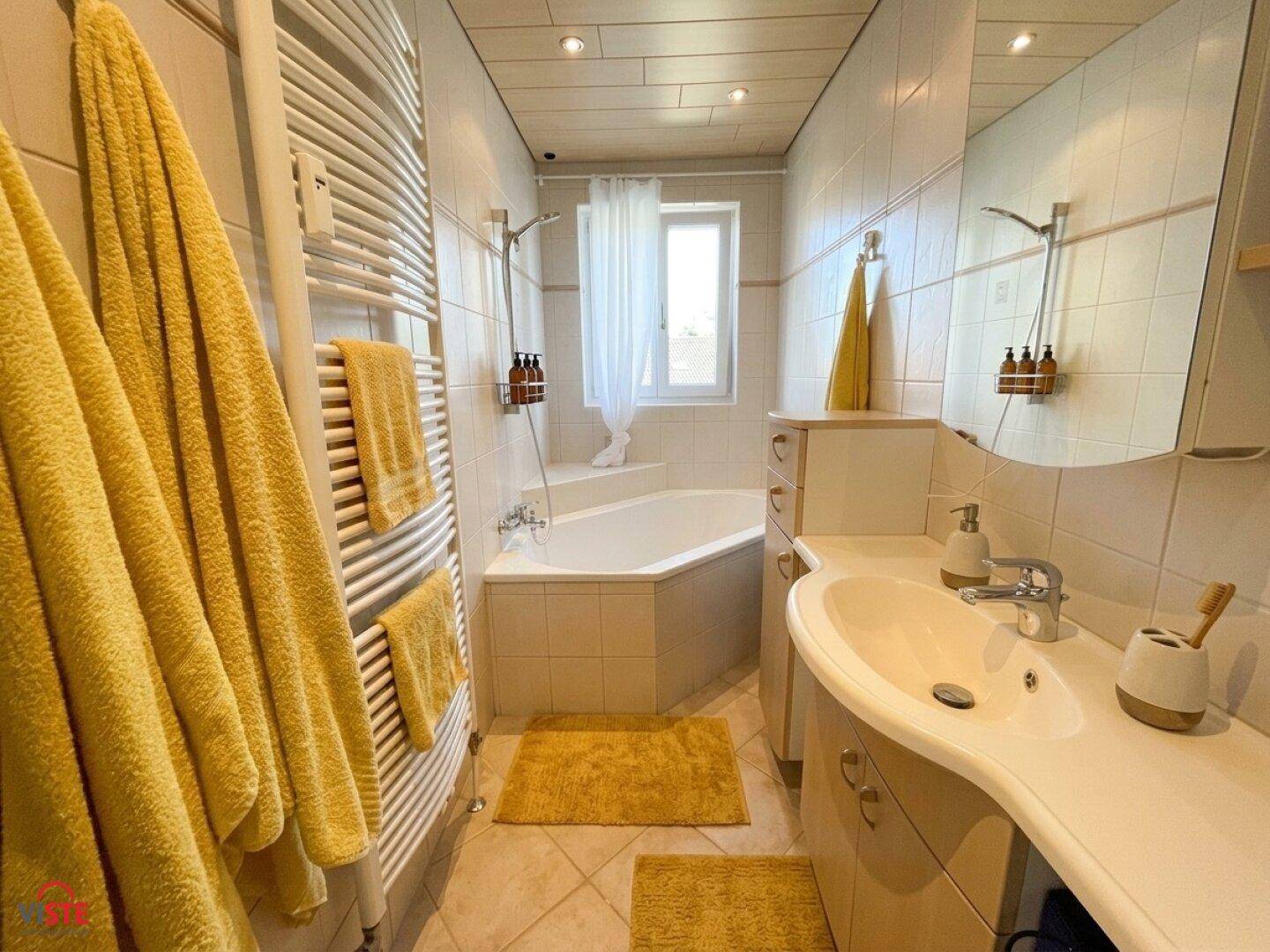 Gefliestes Badezimmer mit Eckbadewanne, Waschtisch und beheiztem Handtuchhalter.