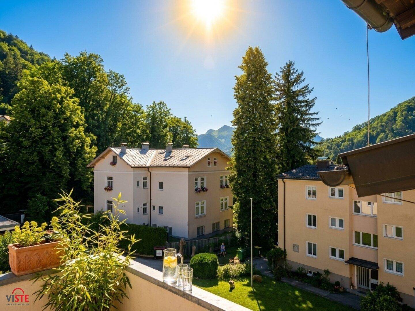 Sonniger Balkon mit Getränken und weitem Blick auf grüne Berge und Gebäude.