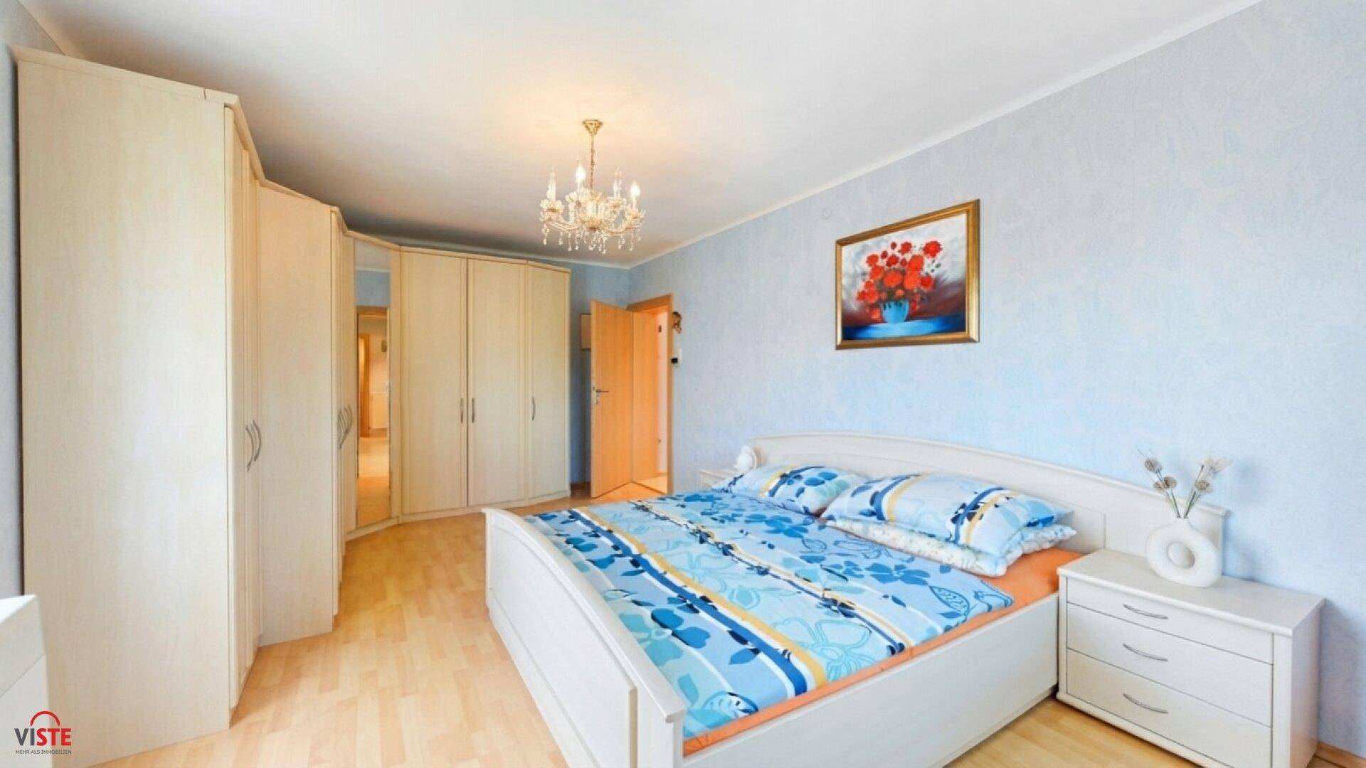 Freundliches Schlafzimmer mit hellem Holzbett, Einbauschränken und blauer Tapete.