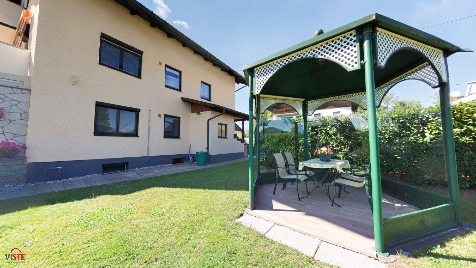 Gepflegter Gartenbereich mit einem grünen Pavillon und Sitzgelegenheiten im Freien.