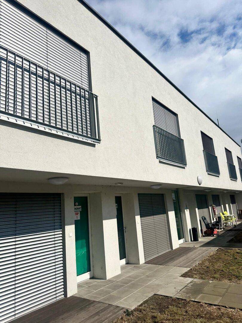 Reihenhausähnliche Fassade mit Balkonen, Rollläden und Zugang zu den Erdgeschosswohnungen.