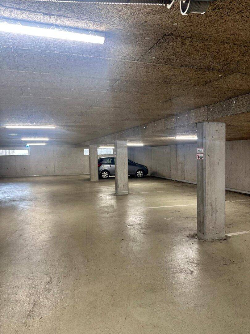 Geräumige Tiefgarage mit Betonstützen und Beleuchtung, ein Auto ist geparkt.