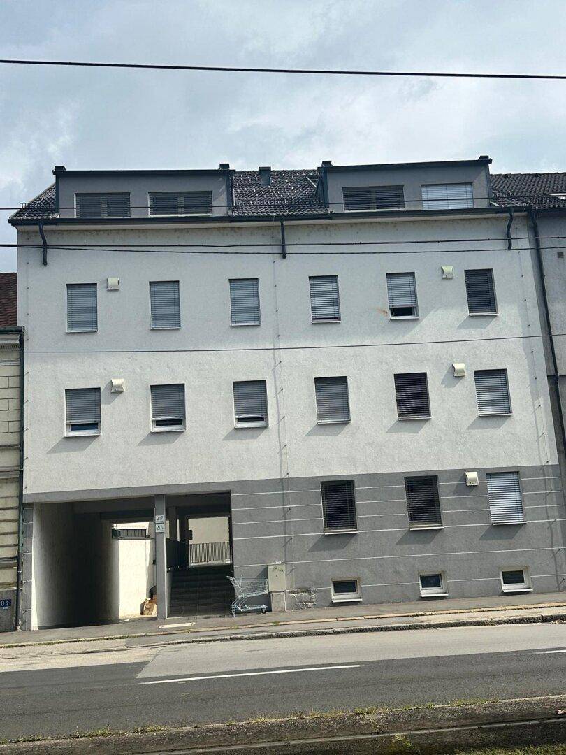Mehrstöckiges Wohnhaus mit weißer und grauer Fassade, vielen Fenstern und Rollläden.