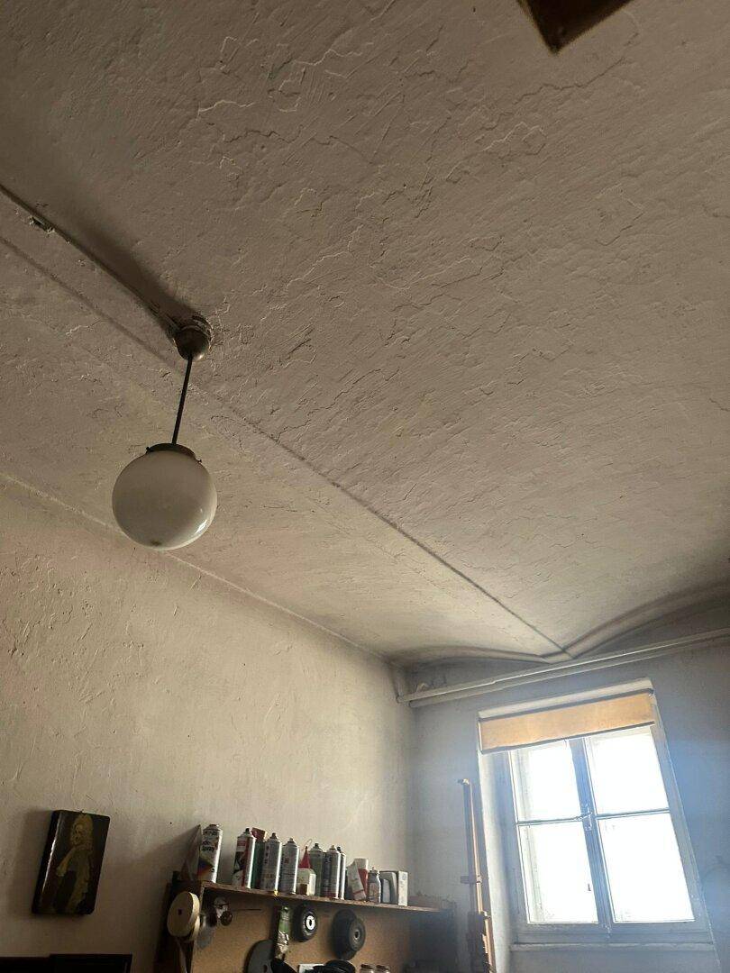 Innenraum mit einfacher Deckenleuchte, einem Fenster und einer Regalwand.