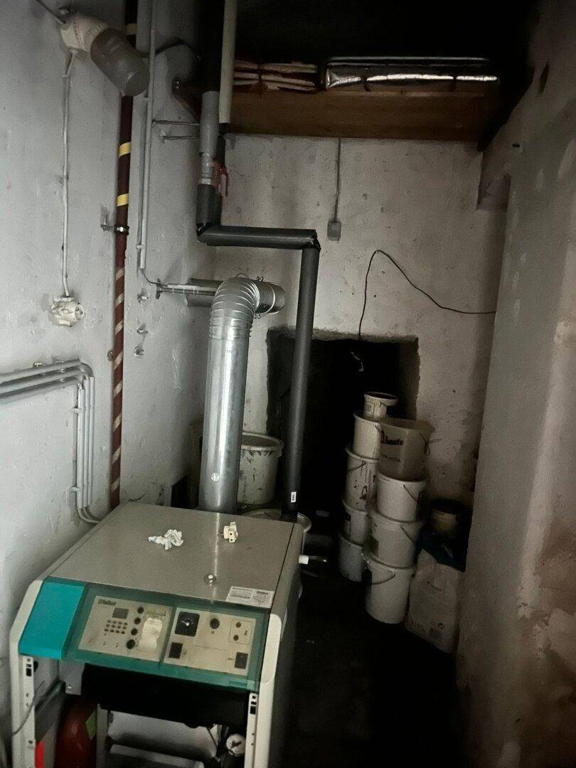 Heizungsraum mit einem Heizkessel, sichtbaren Rohren und Lagerbehältern.