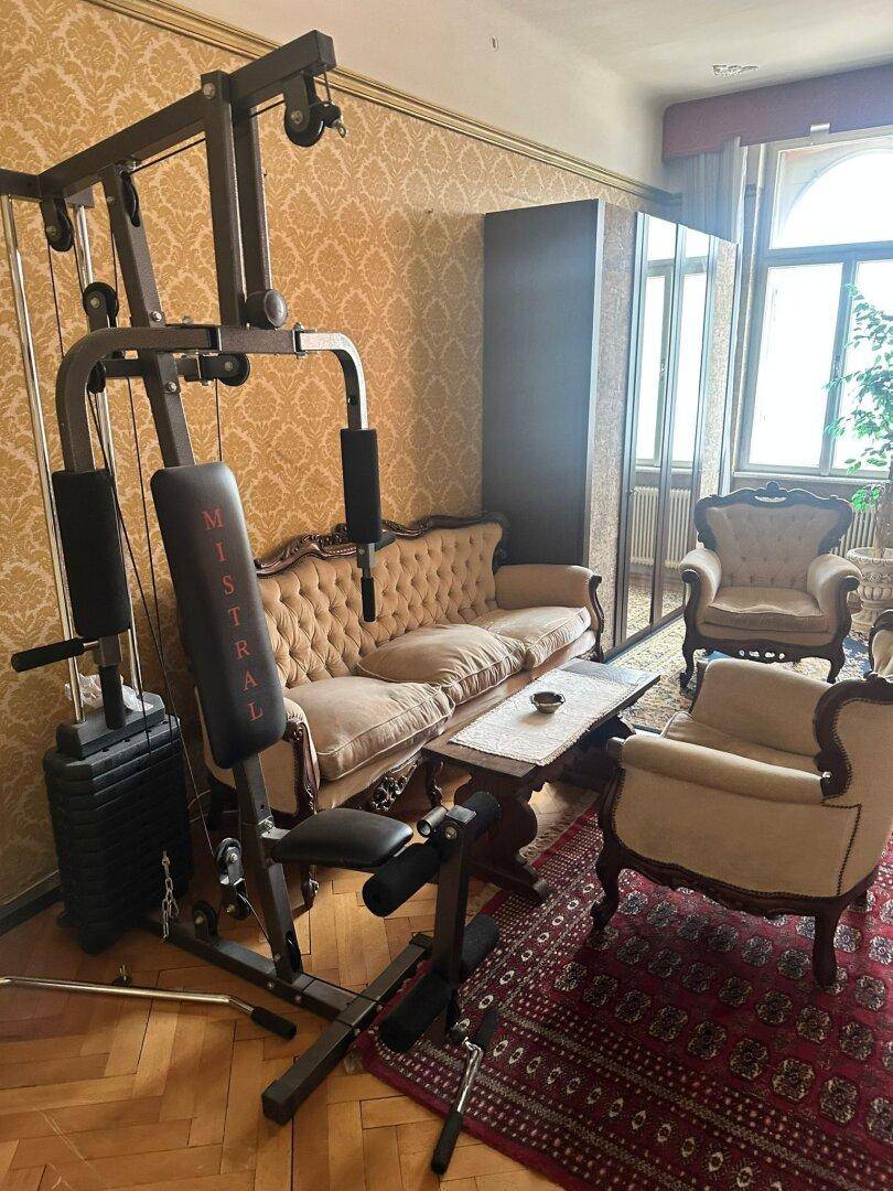 Geräumiges Wohnzimmer mit Fitnessgerät, klassischem Sofa und gemusterten Tapeten.