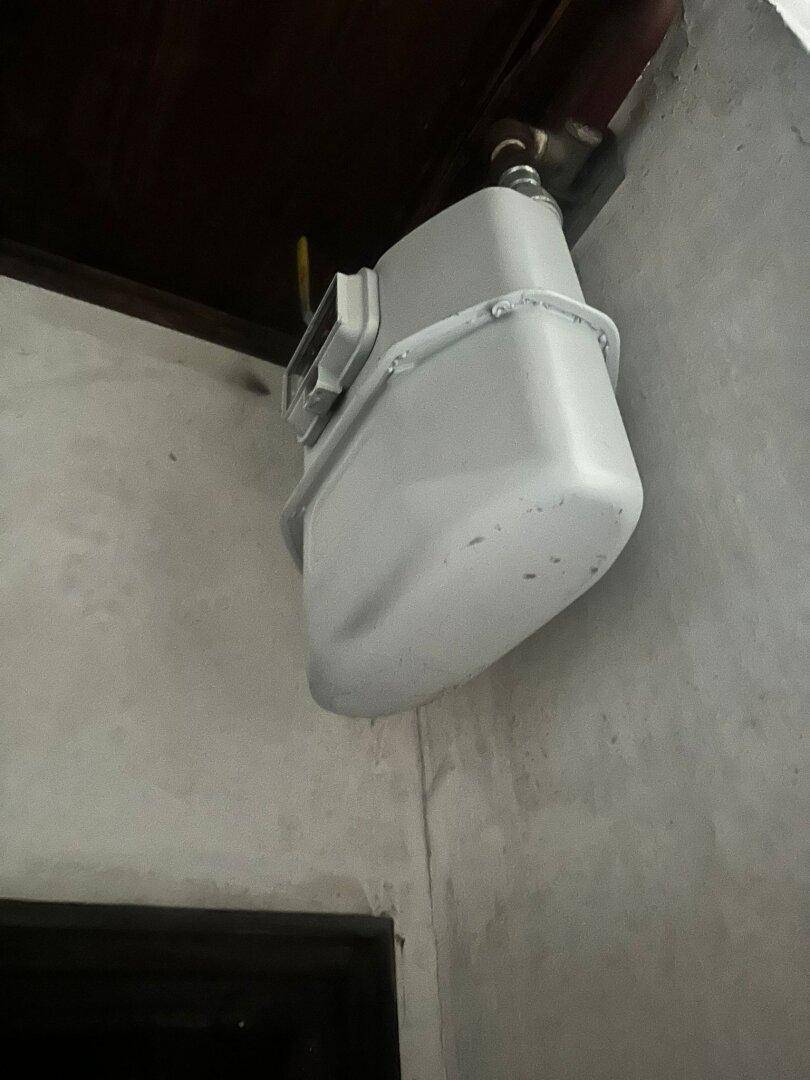 Nahaufnahme eines Gaszählers an einer Wand in einem einfachen Innenraum.