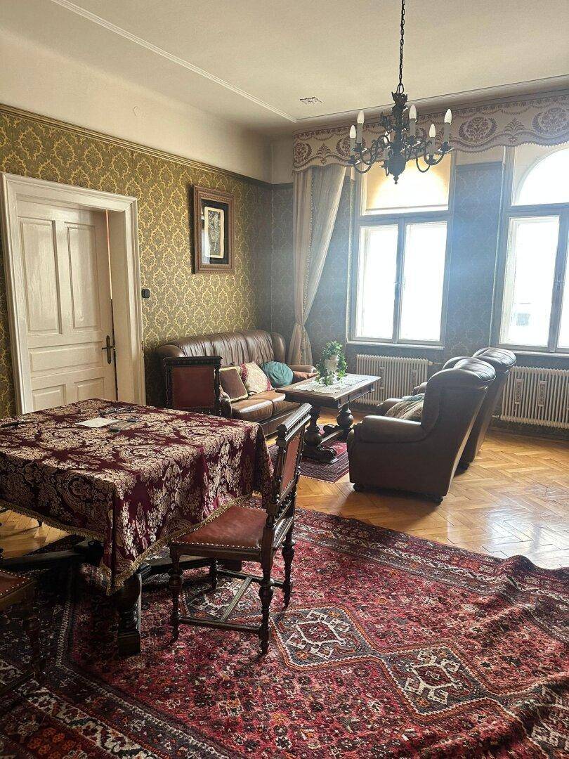 Klassisches Wohnzimmer mit Ledersofa, Esstisch und gemusterten Tapeten.