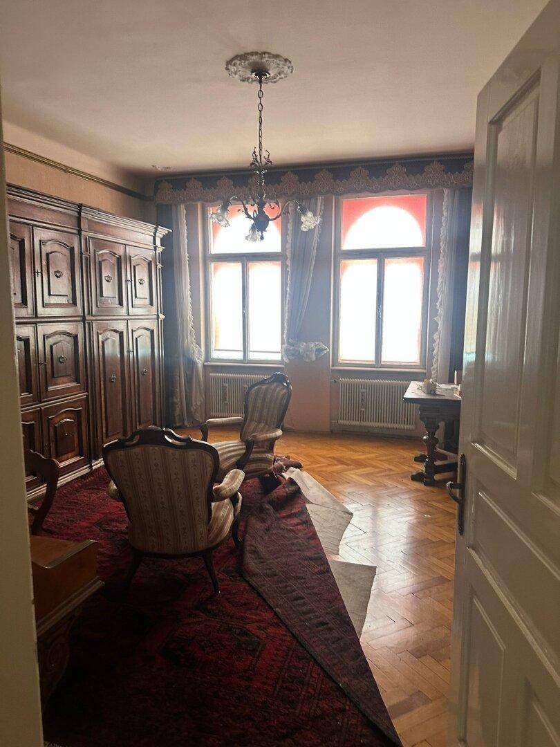 Geräumiges Wohnzimmer mit klassischem Mobiliar, großen Fenstern und Parkettboden.