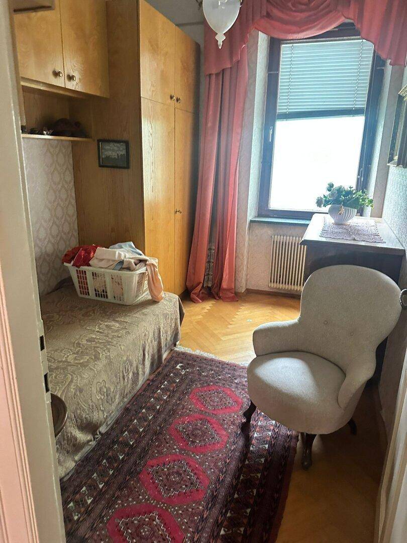 Kleines Schlafzimmer mit Einzelbett, Holzschrank und gemustertem Teppich.