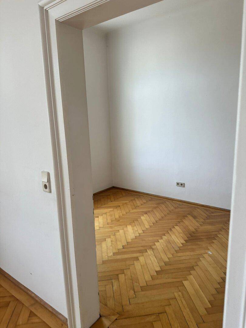 Kleiner, leerer Raum mit Fischgrätparkett und weißen Wänden.