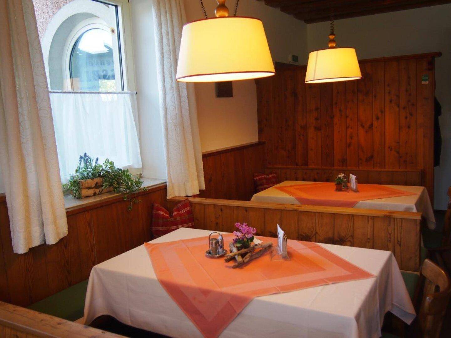 Gemütlicher Restaurantbereich mit traditioneller Holzvertäfelung, Bänken und einem Fenster mit Vorhängen.