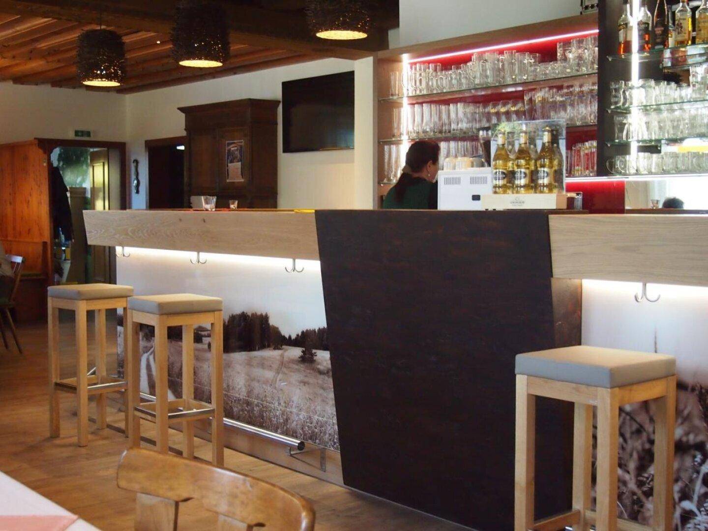 Moderne Bar mit beleuchteter Theke, Barhockern und einer gut bestückten Glasregalwand.